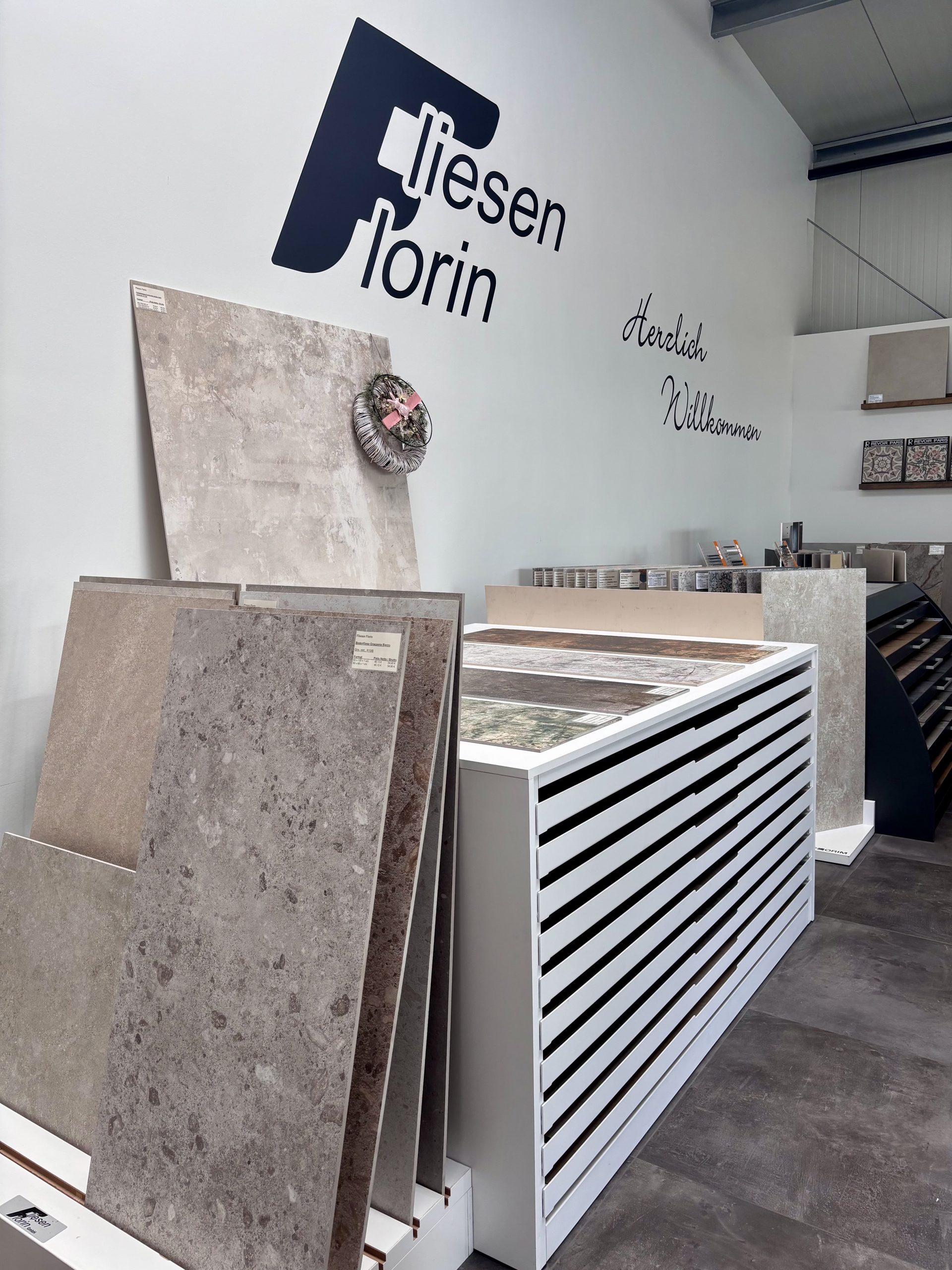Nahaufnahme von großformatigen Fliesenmustern in einem Fliesenausstellungsständer, im Vordergrund eine glänzend weiße und eine rote Fliese.