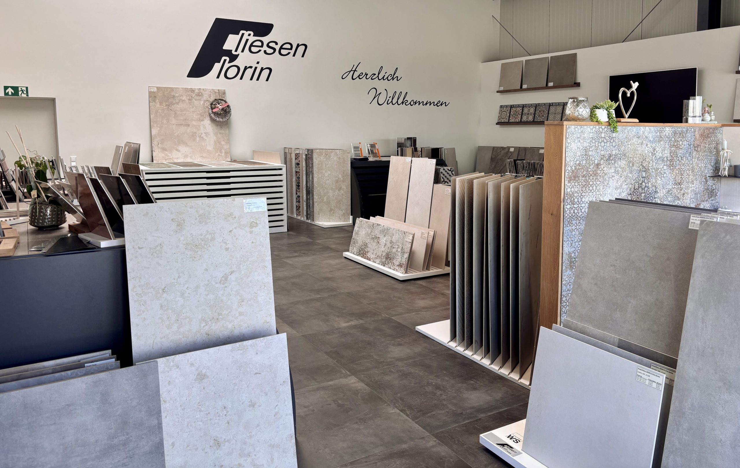 Übersicht über einen modernen Fliesen-Showroom mit großem Ausstellungstisch in der Mitte und verschiedenen Fliesenpräsentationen entlang der Wände.