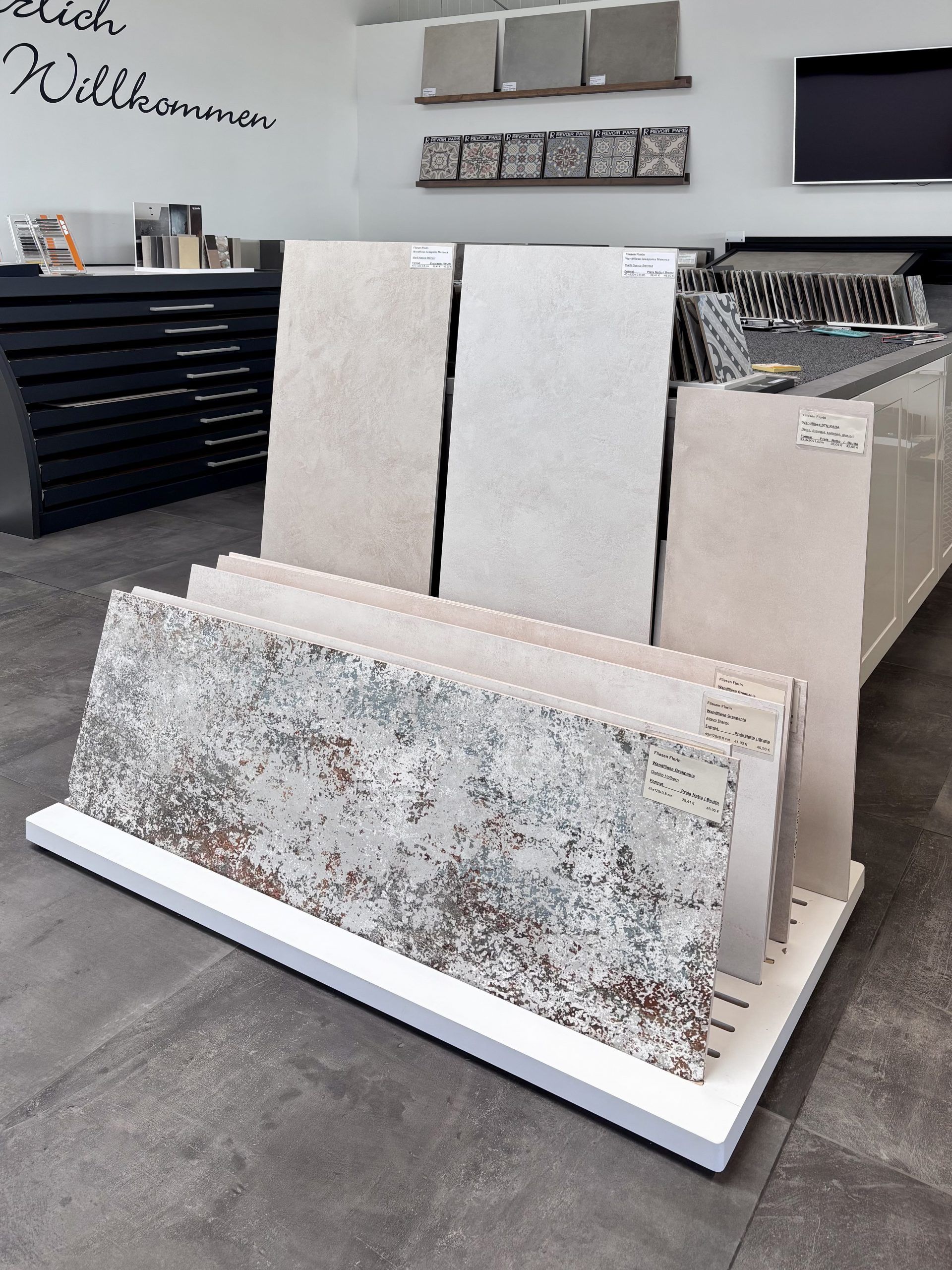 Nahaufnahme von großformatigen Fliesenmustern in einem Fliesenausstellungsständer, im Vordergrund eine glänzend weiße und eine rote Fliese.