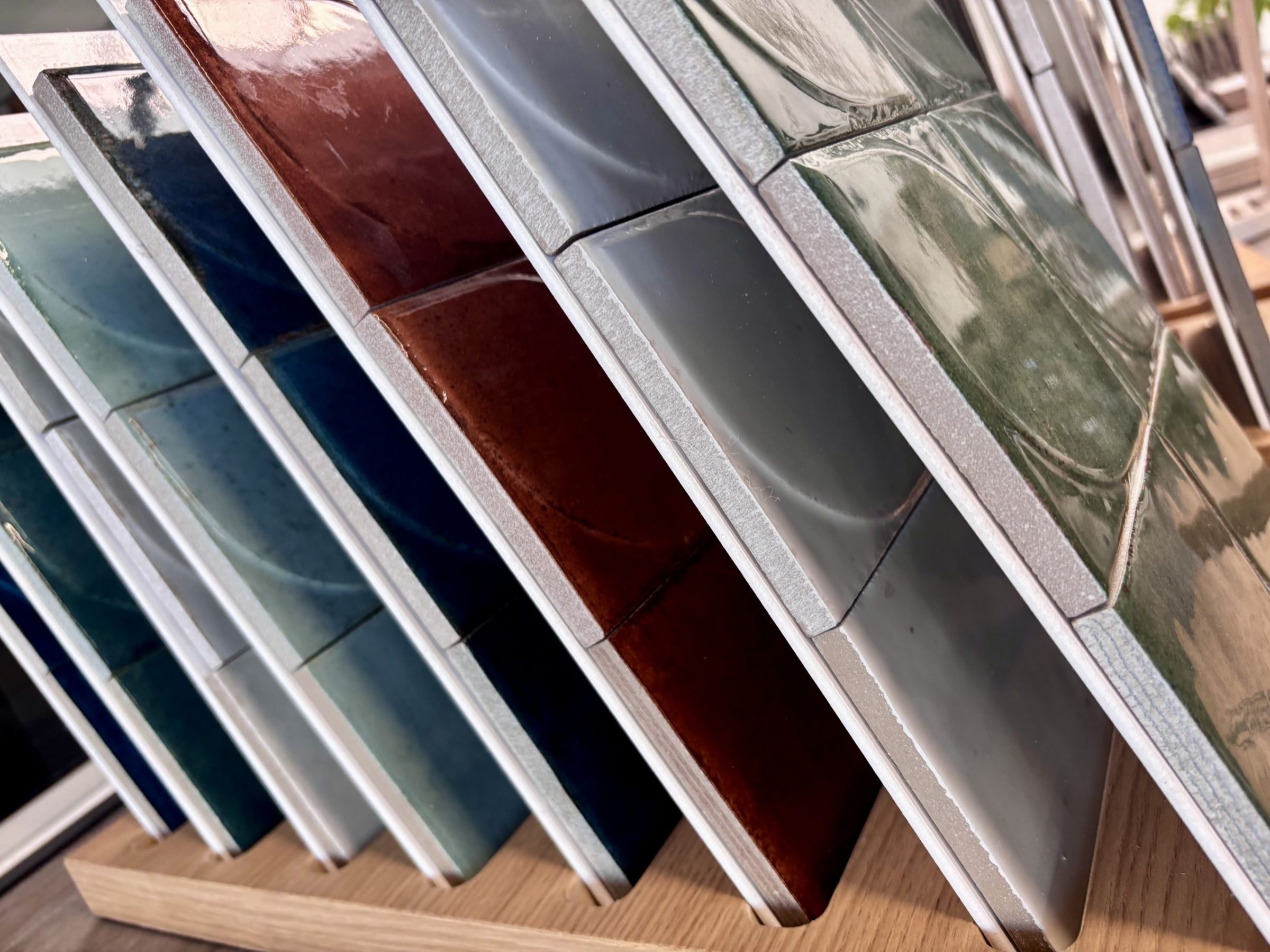 Nahaufnahme von großformatigen Fliesenmustern in einem Fliesenausstellungsständer, im Vordergrund eine glänzend weiße und eine rote Fliese.