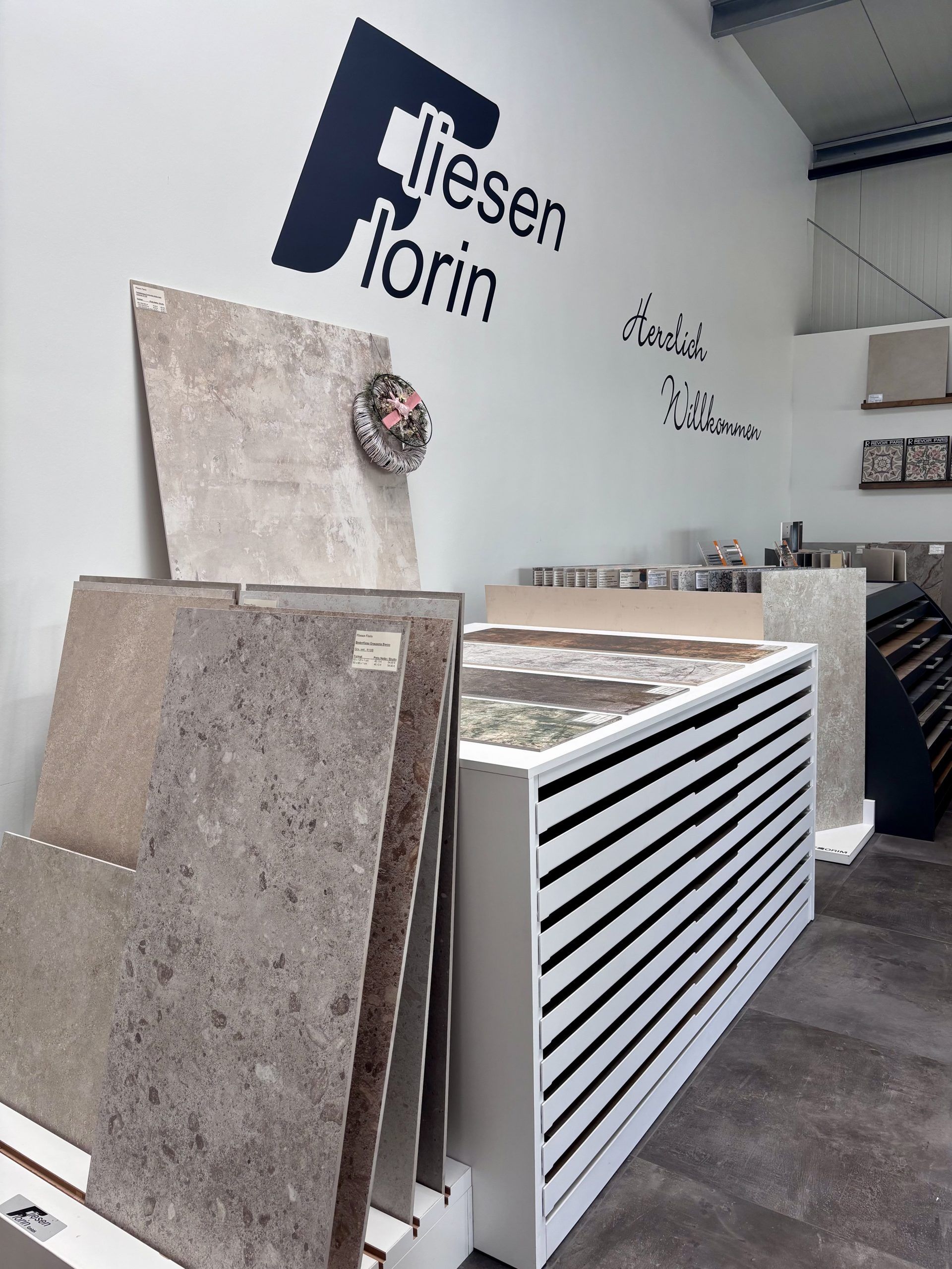 Nahaufnahme von großformatigen Fliesenmustern in einem Fliesenausstellungsständer, im Vordergrund eine glänzend weiße und eine rote Fliese.