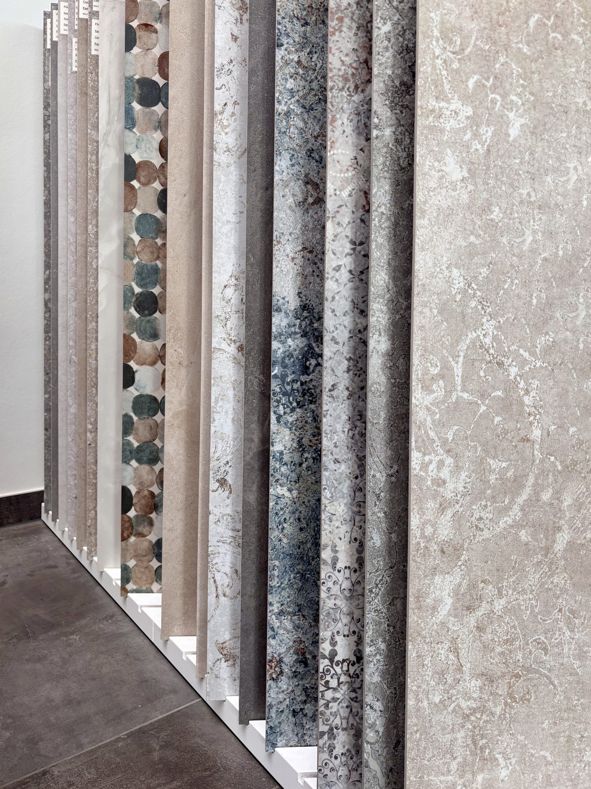 Nahaufnahme von großformatigen Fliesenmustern in einem Fliesenausstellungsständer, im Vordergrund eine glänzend weiße und eine rote Fliese.