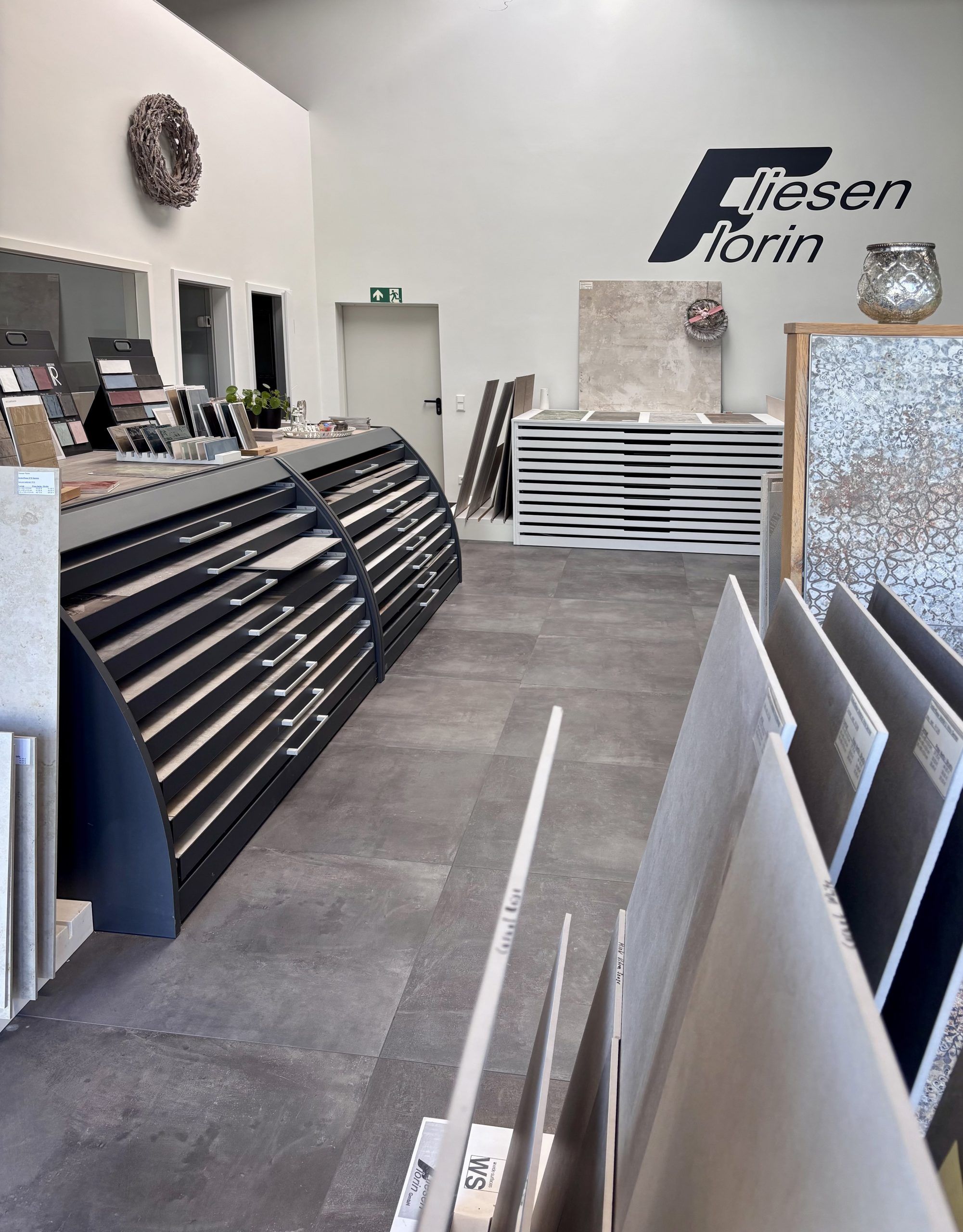 Nahaufnahme von großformatigen Fliesenmustern in einem Fliesenausstellungsständer, im Vordergrund eine glänzend weiße und eine rote Fliese.