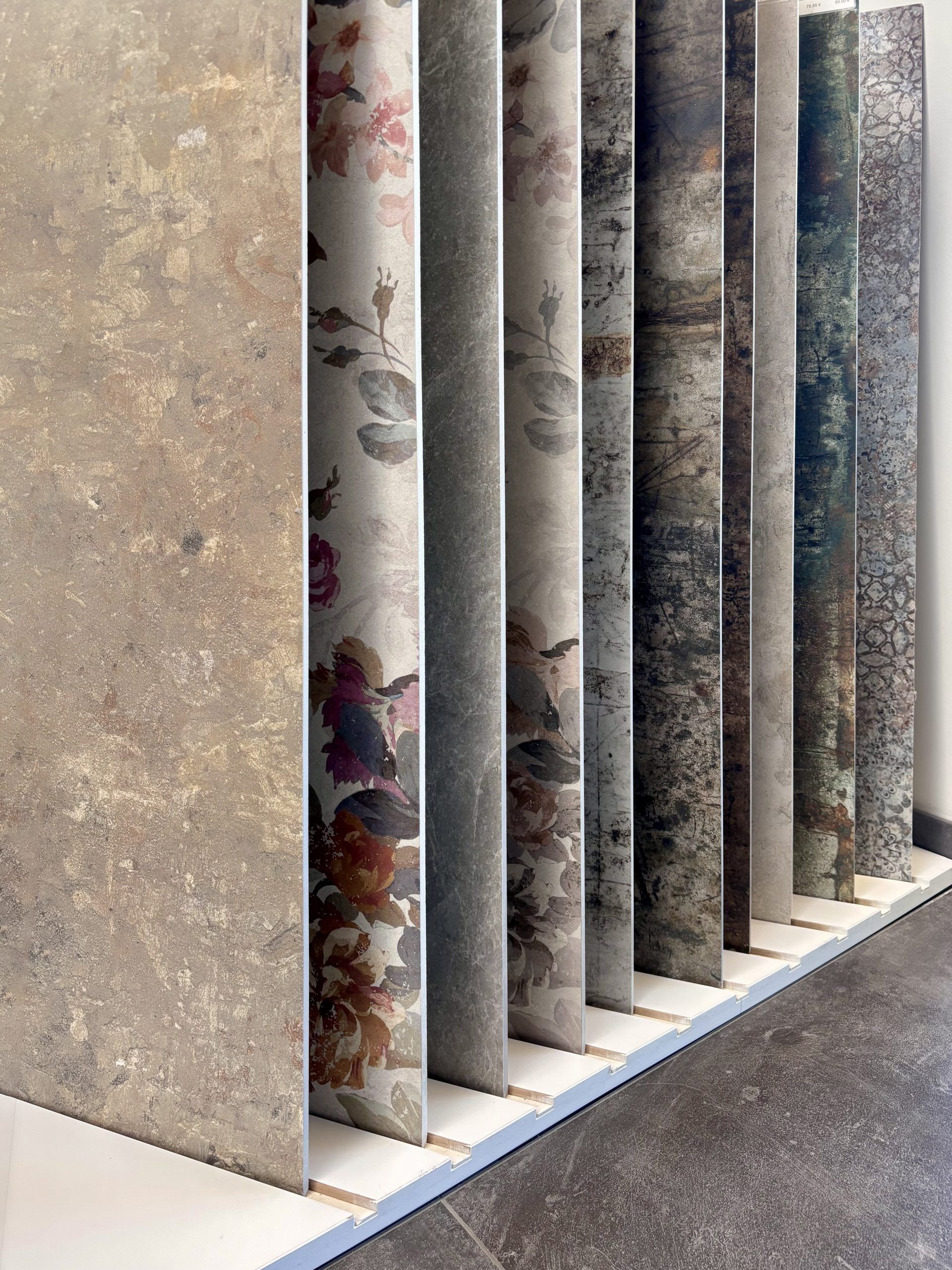 Nahaufnahme von großformatigen Fliesenmustern in einem Fliesenausstellungsständer, im Vordergrund eine glänzend weiße und eine rote Fliese.