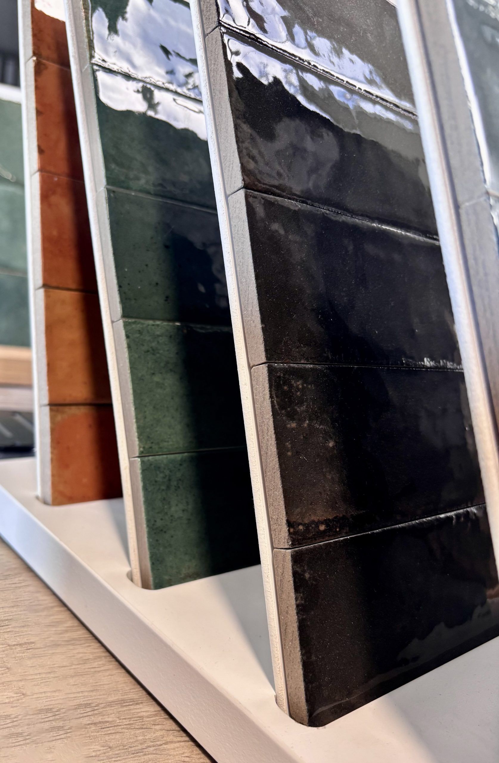 Nahaufnahme von großformatigen Fliesenmustern in einem Fliesenausstellungsständer, im Vordergrund eine glänzend weiße und eine rote Fliese.