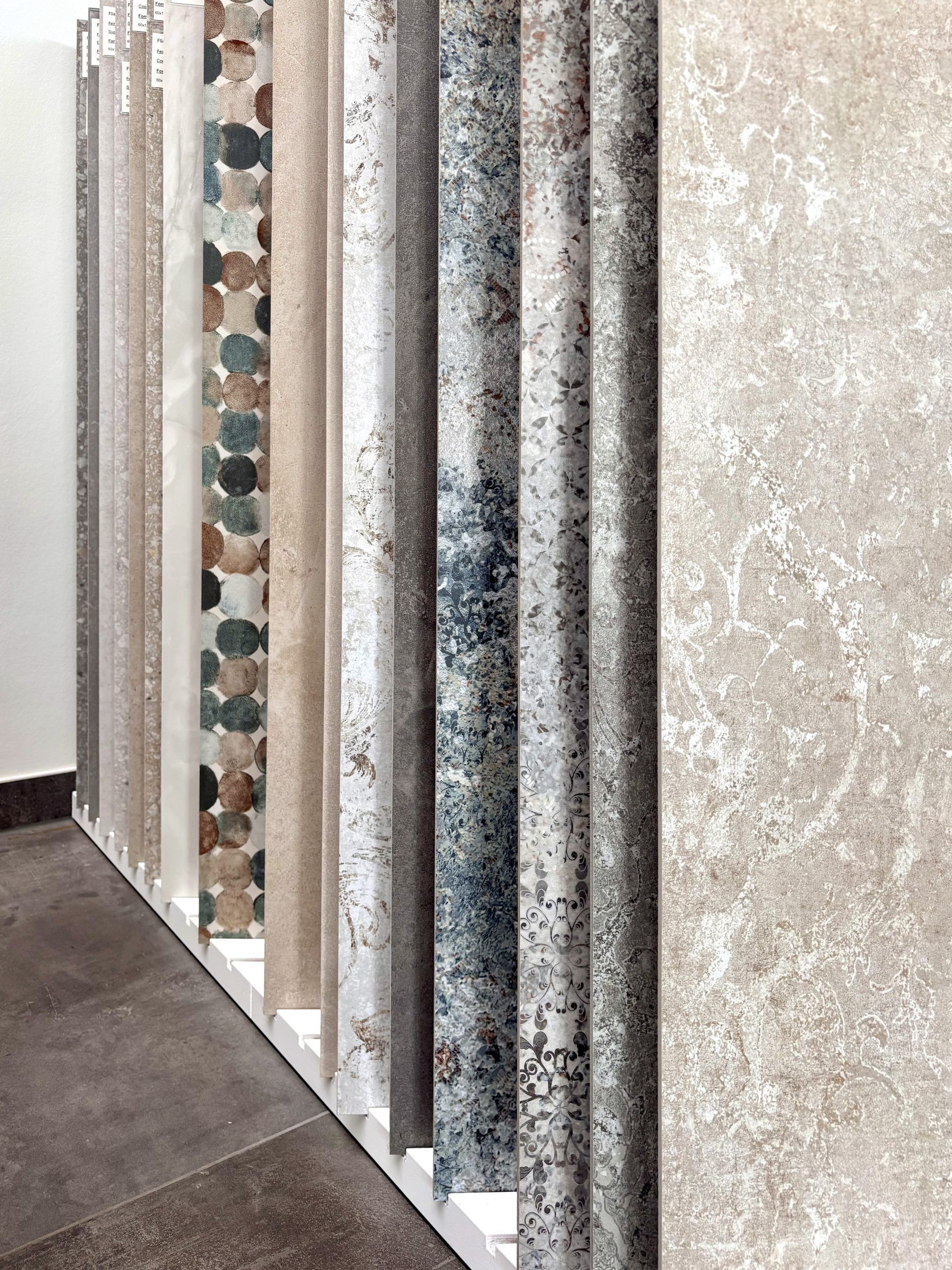 Nahaufnahme von großformatigen Fliesenmustern in einem Fliesenausstellungsständer, im Vordergrund eine glänzend weiße und eine rote Fliese.